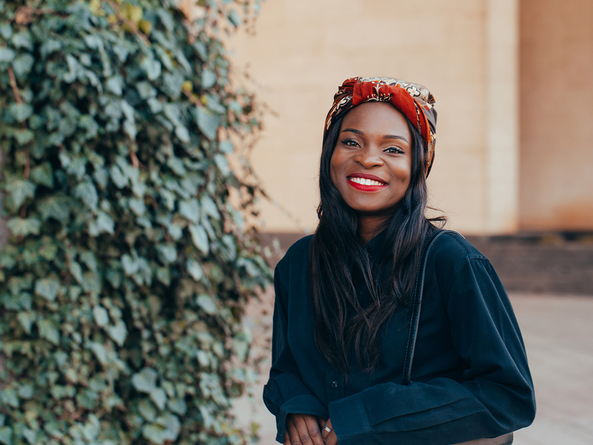 African-American woman smiling and wearing a hair scarf.